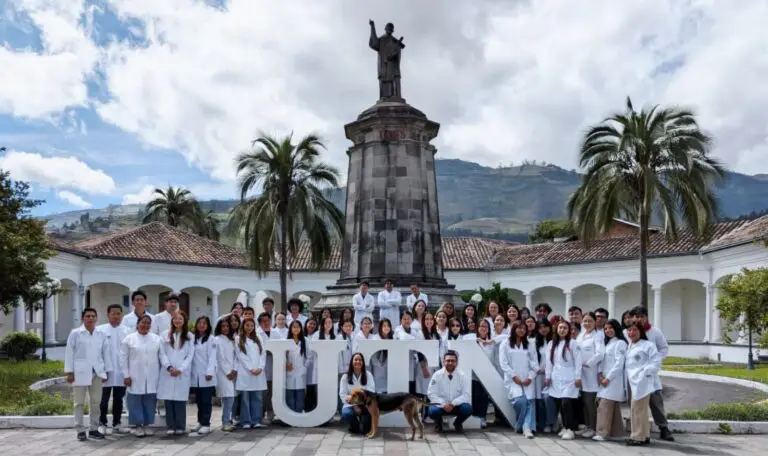Foto di gruppo con un cane di circa 50 ricercatori dell'Università di Ibarra in Ecuador. Tutti indossano camici bianchi e sono davanti a un monumento con una statua benedicente.