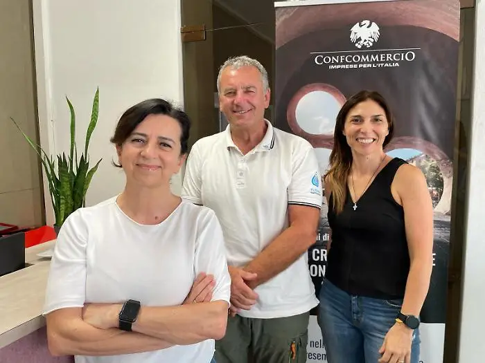 Gruppo composto da due donne e un uomo - Mario Guerrieri, CEO di Nutrevo Q.E.- sorridenti, in abbigliamento estivo, davanti a un banner di Confcommercio in occasione di un evento sull'agricoltura biologica.